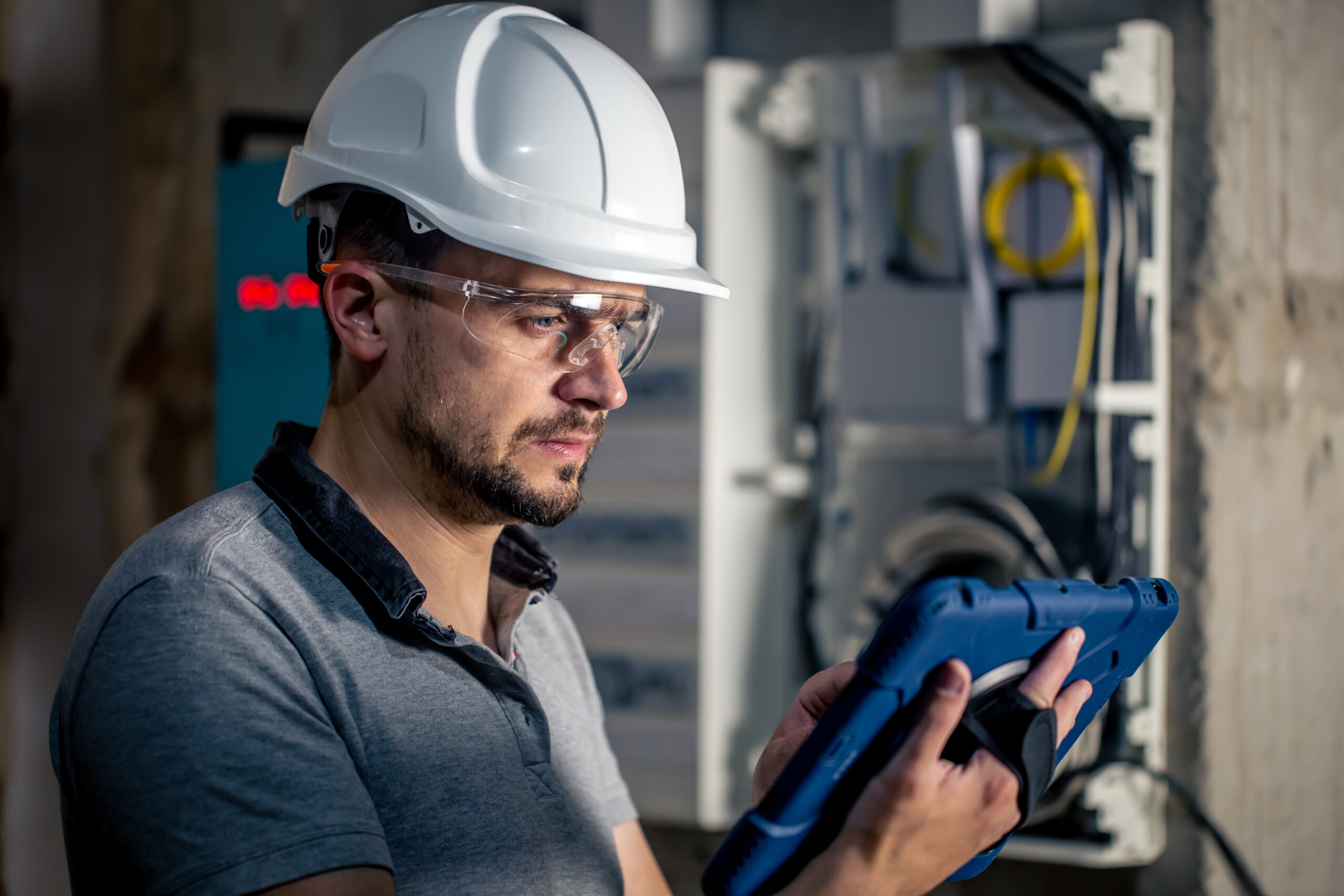 Man, an electrical technician working in a switchboard with fuses. Installation and connection of electrical equipment. Professional uses a tablet. electricien qualifelec Lyon Pro Garantie Assurance Conseil expert certifié